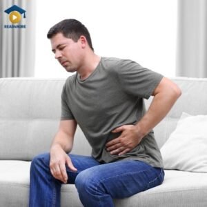A man sits on a couch holding his stomach in pain, illustrating a symptom that is abnormal or 'not normal'. This image is a visual aid for an OET medical English glossary on read4more.com, helping healthcare professionals learn vocabulary for patient consultations and OET speaking tasks.