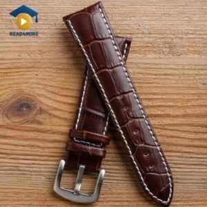 A high-quality photo of a brown leather watch band with a crocodile texture and a silver buckle, lying on a wooden surface. This image is a vocabulary aid for a read4more.com beginner English lesson.