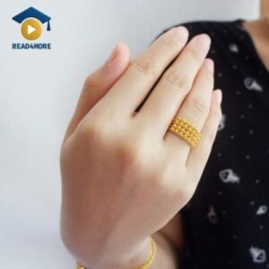 A close-up photo of a woman's hand wearing an intricate, textured golden ring. This image is a visual aid from read4more.com, used to teach beginner English students the adjective for the color of gold.