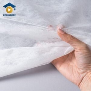 A hand holds and feels a piece of soft, white fabric, visually representing the English vocabulary word 'material'. This image is from a read4more.com lesson for beginners on how to describe what things are made of.