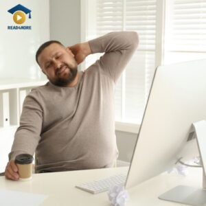 A man rubs his neck in pain while sitting at his office computer, illustrating the negative effects of a sedentary lifestyle. This image from read4more.com is for a vocabulary lesson on health and wellness for IELTS and OET students.