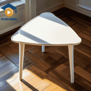 A modern, white side table with a triangular top and three legs, sitting on a wooden floor. This image is a visual aid from read4more.com for a beginner's English lesson on how to describe shapes.