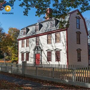 A large house with a white fence, visually defining the English verb "live" (to have your home in a place) for the Read4More online vocabulary glossary.