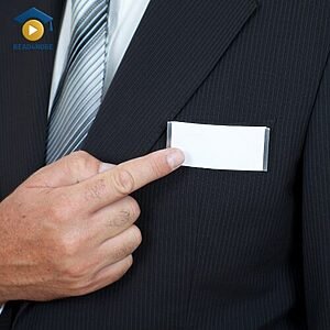 A person in a suit pointing to a blank name tag, visually illustrating the concept of a "name" (what people call you) for the Read4More online vocabulary glossary.