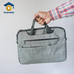 A hand holding a grey carry-on bag (briefcase style) against a white background, visually defining the English vocabulary word for a small bag taken on a plane for the Read4More online glossary.